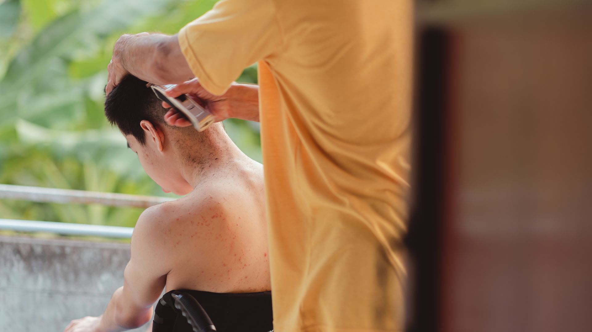 A man is getting his hair cut by a man in a yellow shirt.