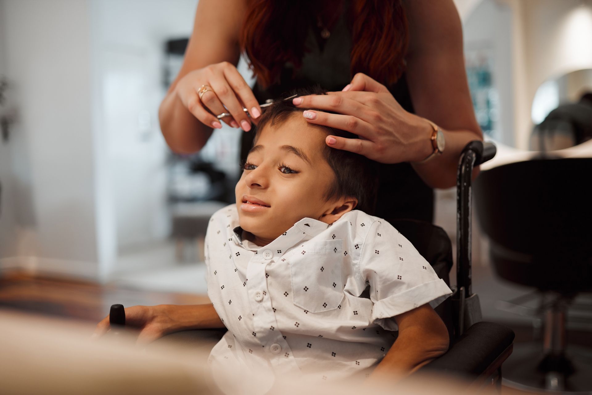A woman is cutting a young boy 's hair in a salon.