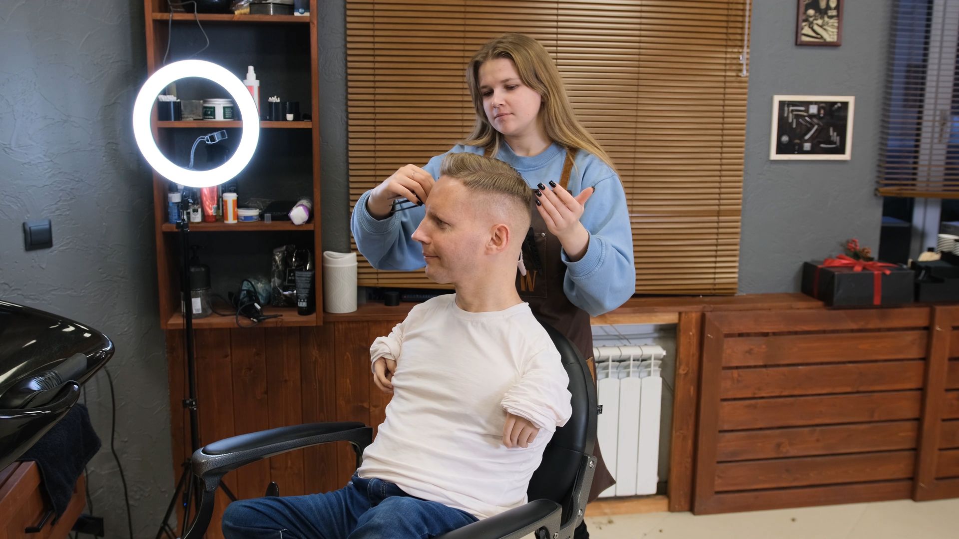 A woman is cutting a man 's hair in a barber shop.