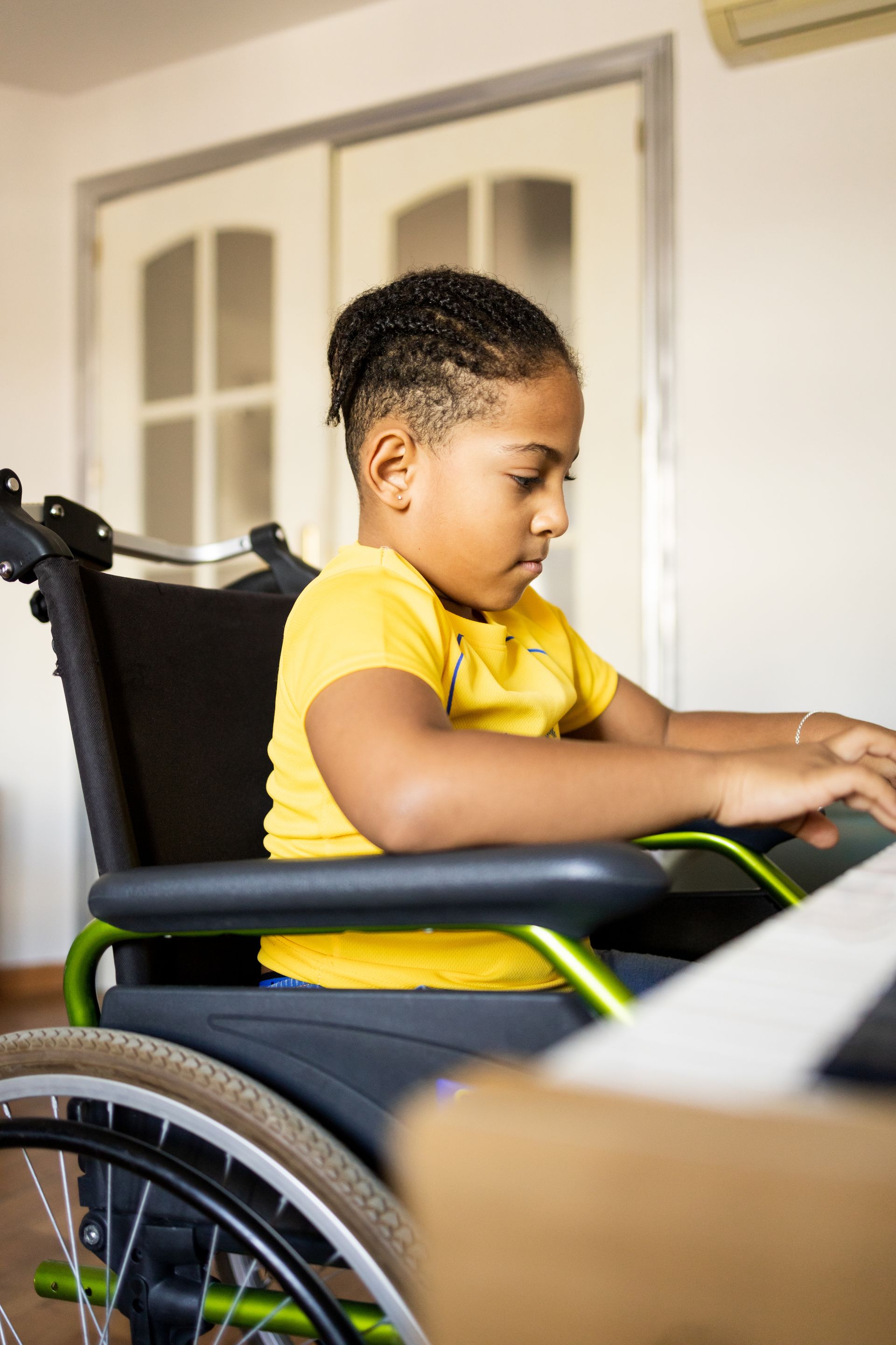 A young boy in a wheelchair is using a laptop computer.