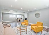 Bright modern living room with white walls, gray sofa, yellow chairs, and a round mirror on the wall