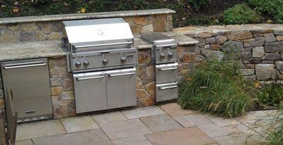 A stainless steel grill is built into a stone wall.