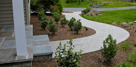 A brick walkway leading to a house with a lush green lawn.
