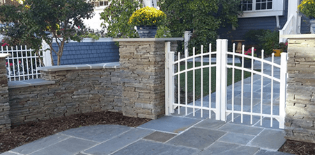 A white gate is sitting in front of a stone wall.