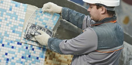 A man is laying tiles on a wall.