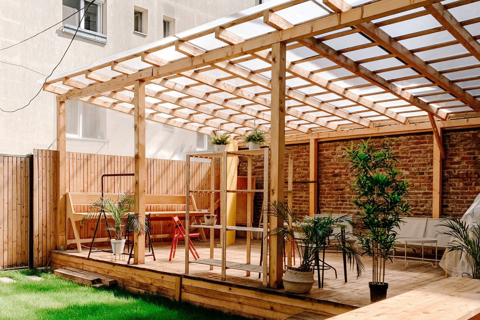 A wooden pergola with a clear roof is in a backyard.