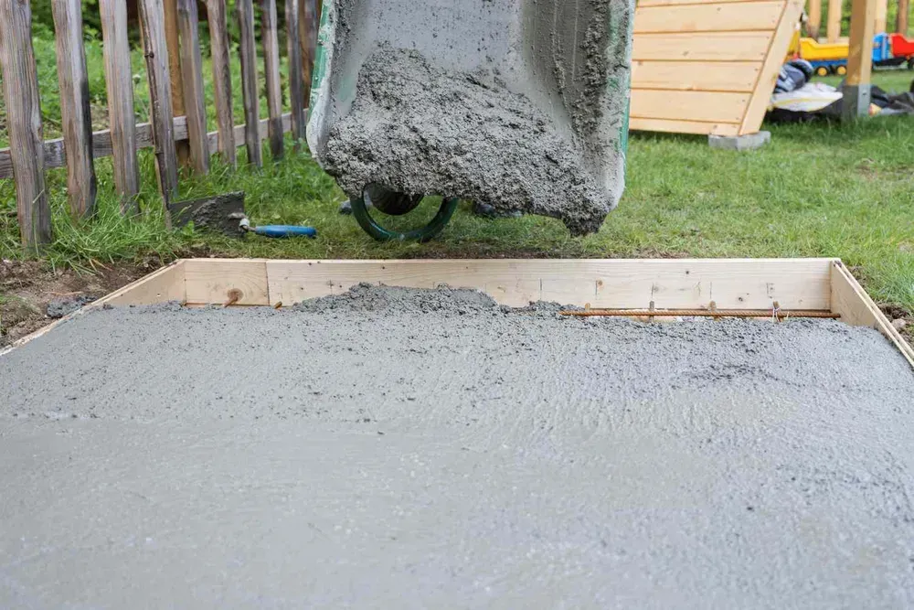 A person is pouring concrete into a wooden frame.