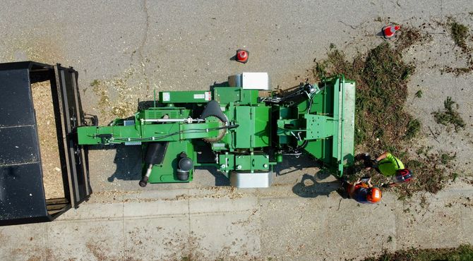 Top-down view of a green farm machine on gravel beside a black truck bed and scattered tools