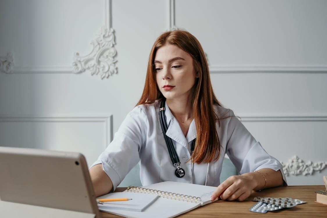 Medical doctor working behind a desk with a laptop, medicine, and a notebook