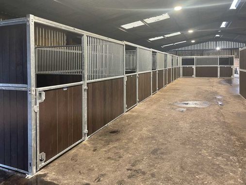 A row of horse stables with wooden walls and metal fences.