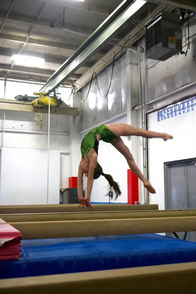 a woman is doing a handstand on a balance beam in a gym