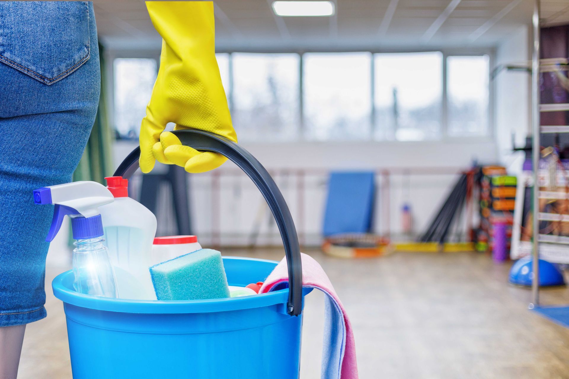 a person wearing yellow gloves is holding a blue bucket filled with cleaning supplies