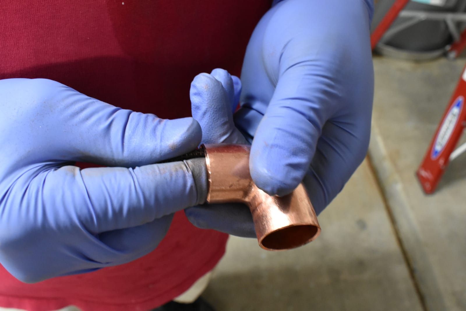 Plumber wearing blue gloves holds copper pipe and elbow fitting working on a hot water heater.