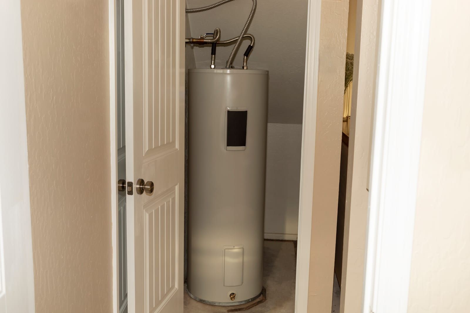 A tall water heater in a narrow closet with an open door.