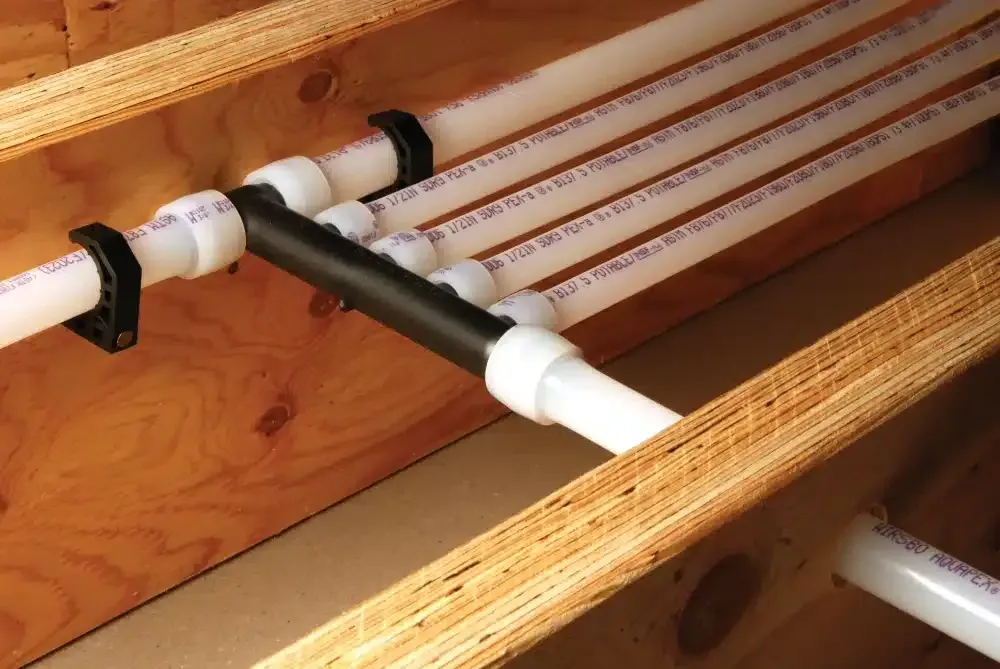 Pipes connected with white and black fittings, secured with black clips, against wooden framing.