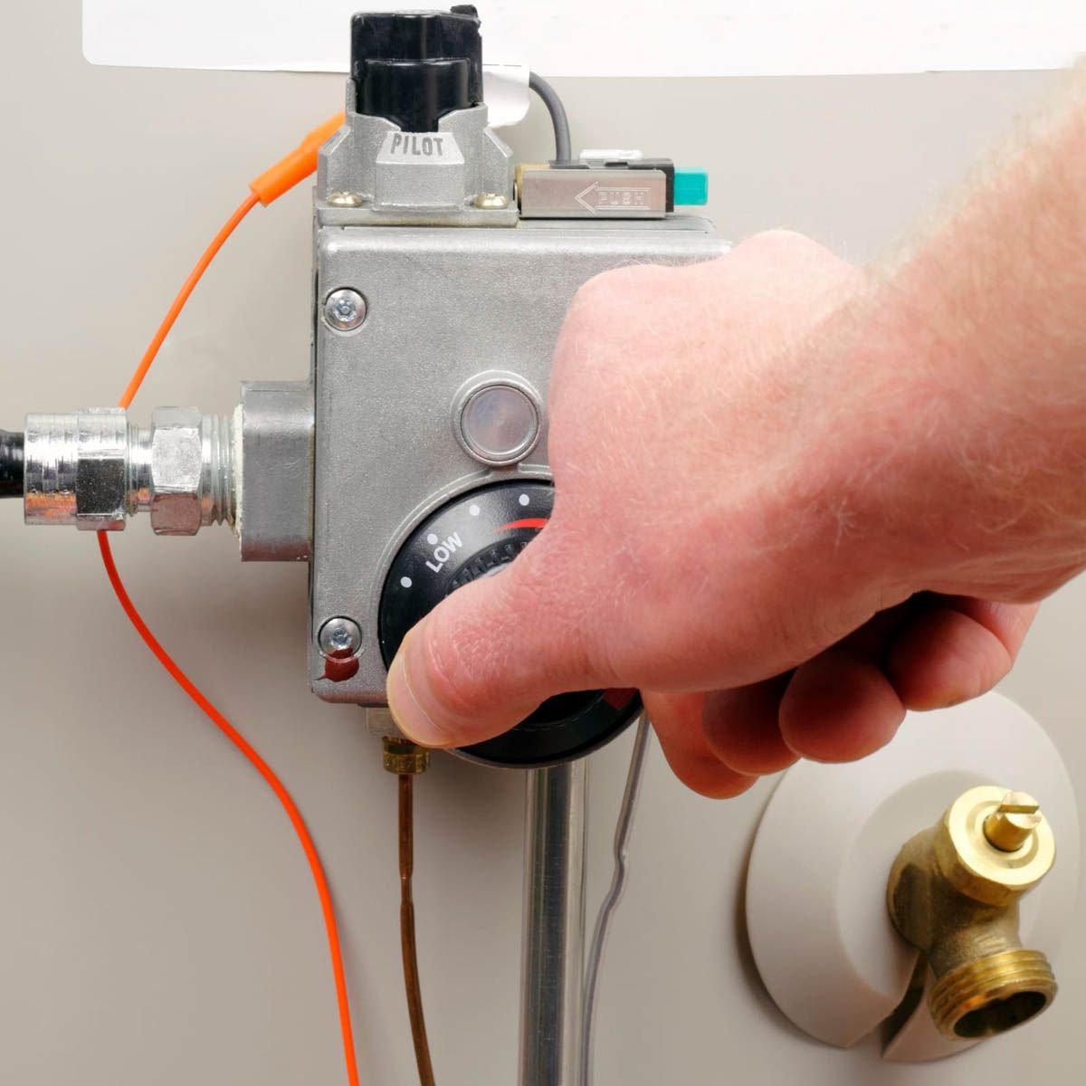 Hand turning a black dial on a water heater, adjusting the temperature.