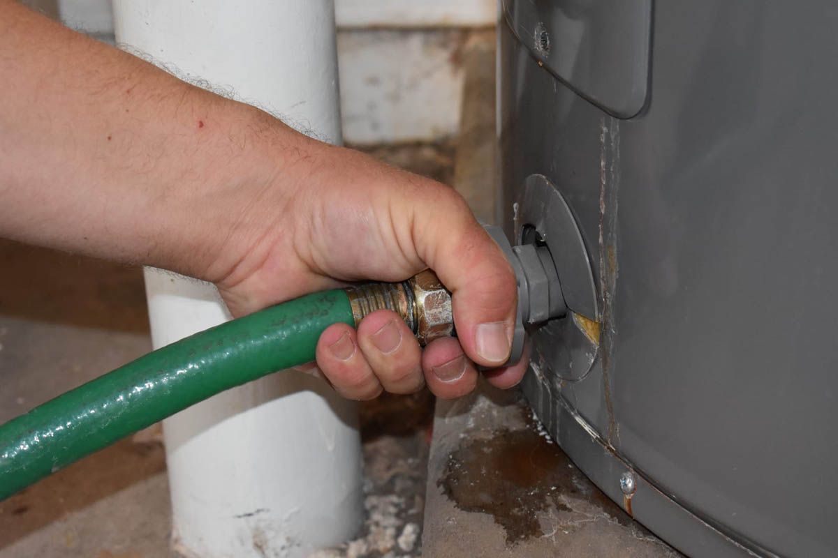 Person attaching green hose to drain valve of a water heater.
