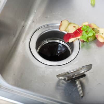 Stainless steel kitchen sink with food scraps partially covering the drain.