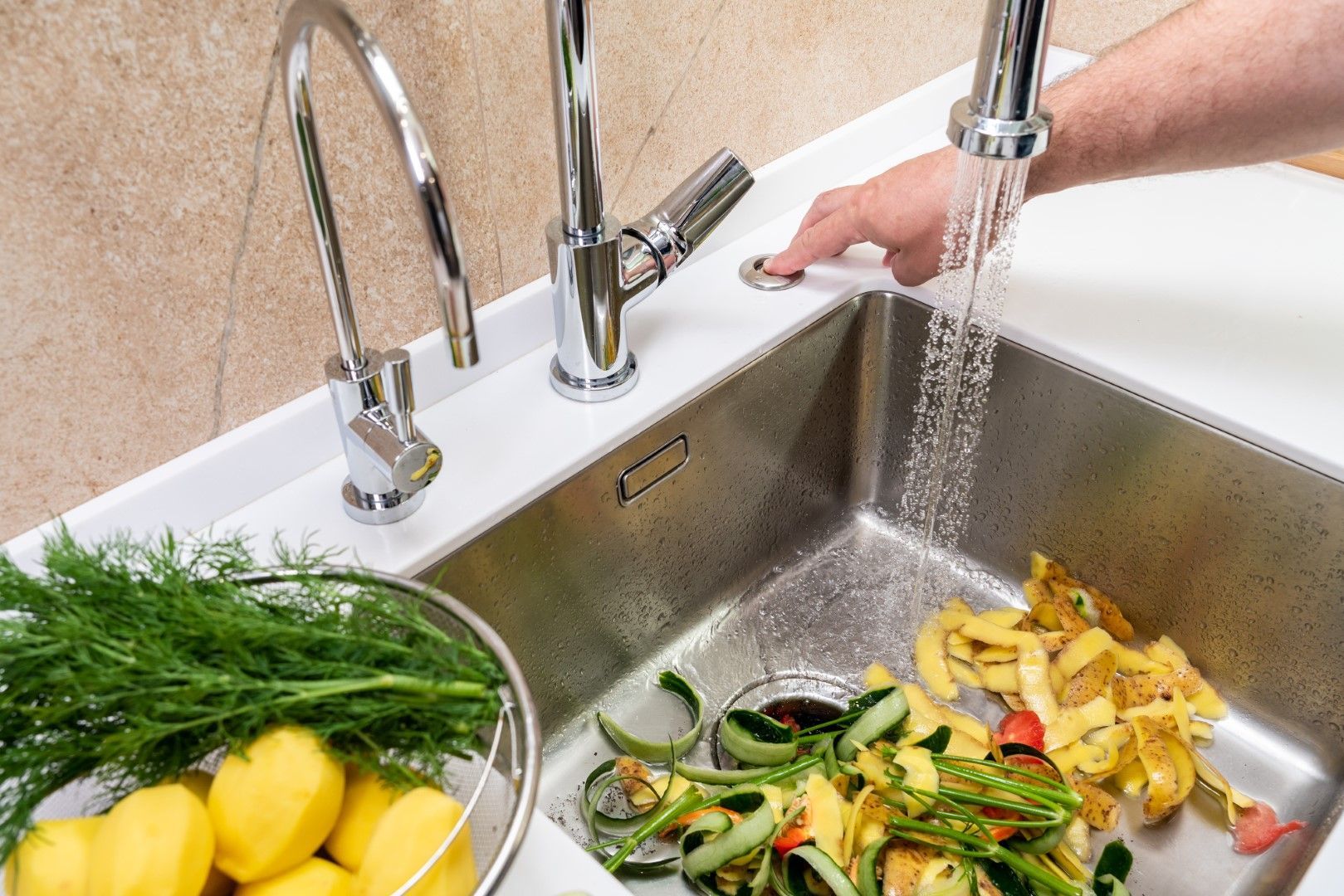 Hand activating faucet, water running into a sink with food scraps and vegetables.