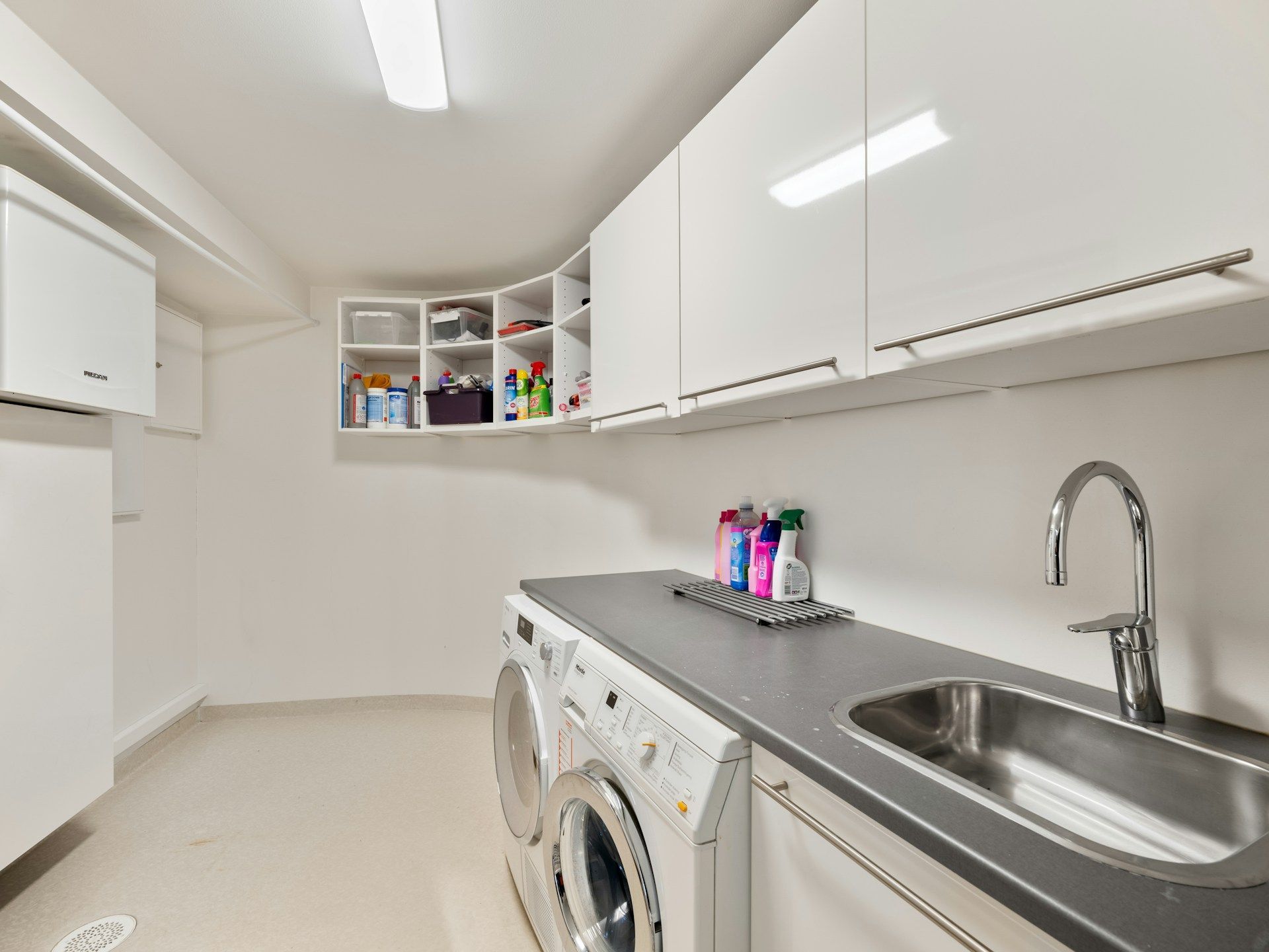Laundry room with white cabinets, washer/dryer, sink, and cleaning supplies.
