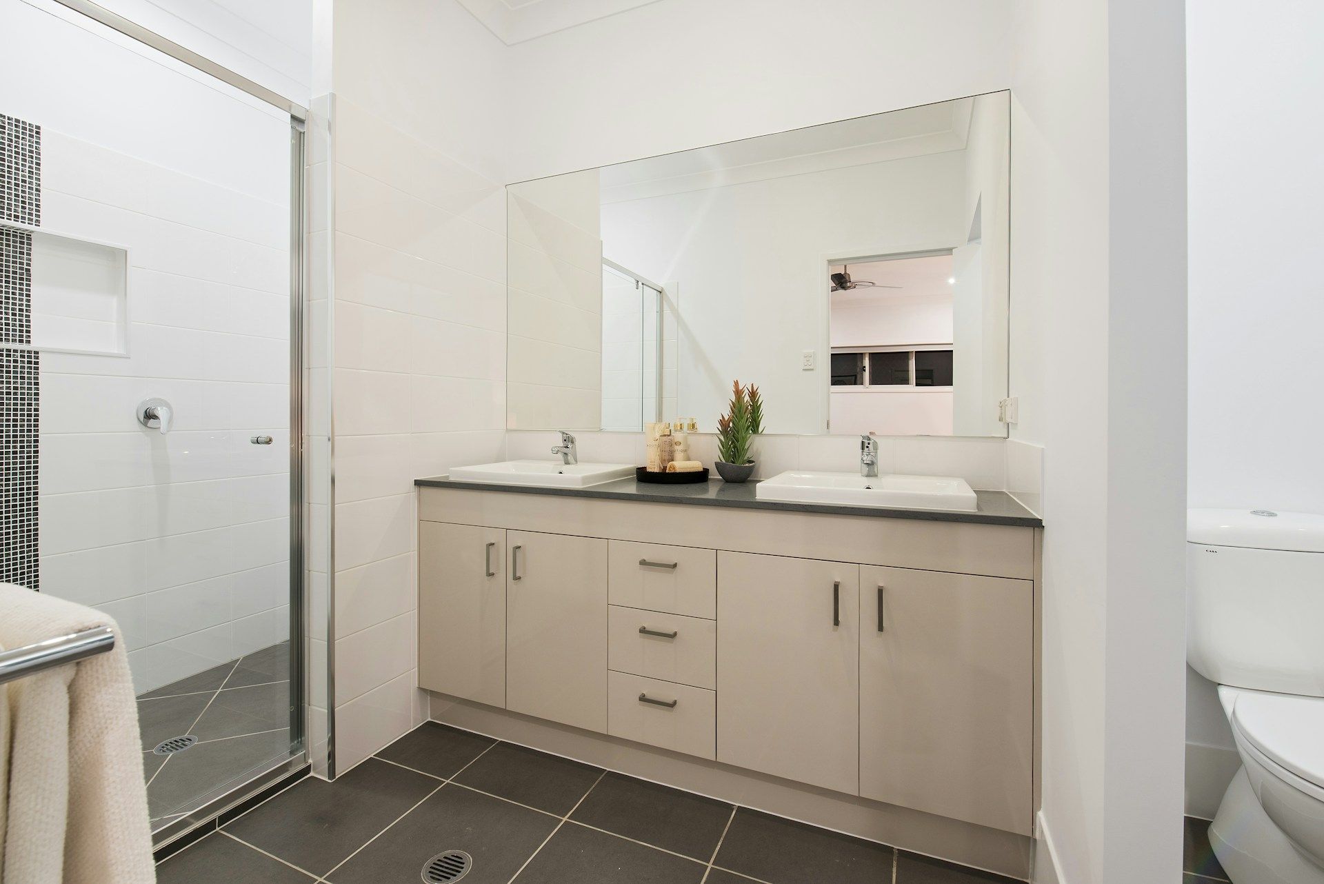 Bathroom with a large mirror over a double vanity, shower, and toilet. Gray and white color scheme.