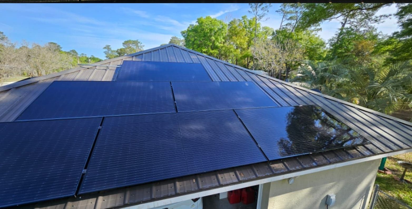 Solar panels on a metal roof against a blue sky, surrounded by trees.