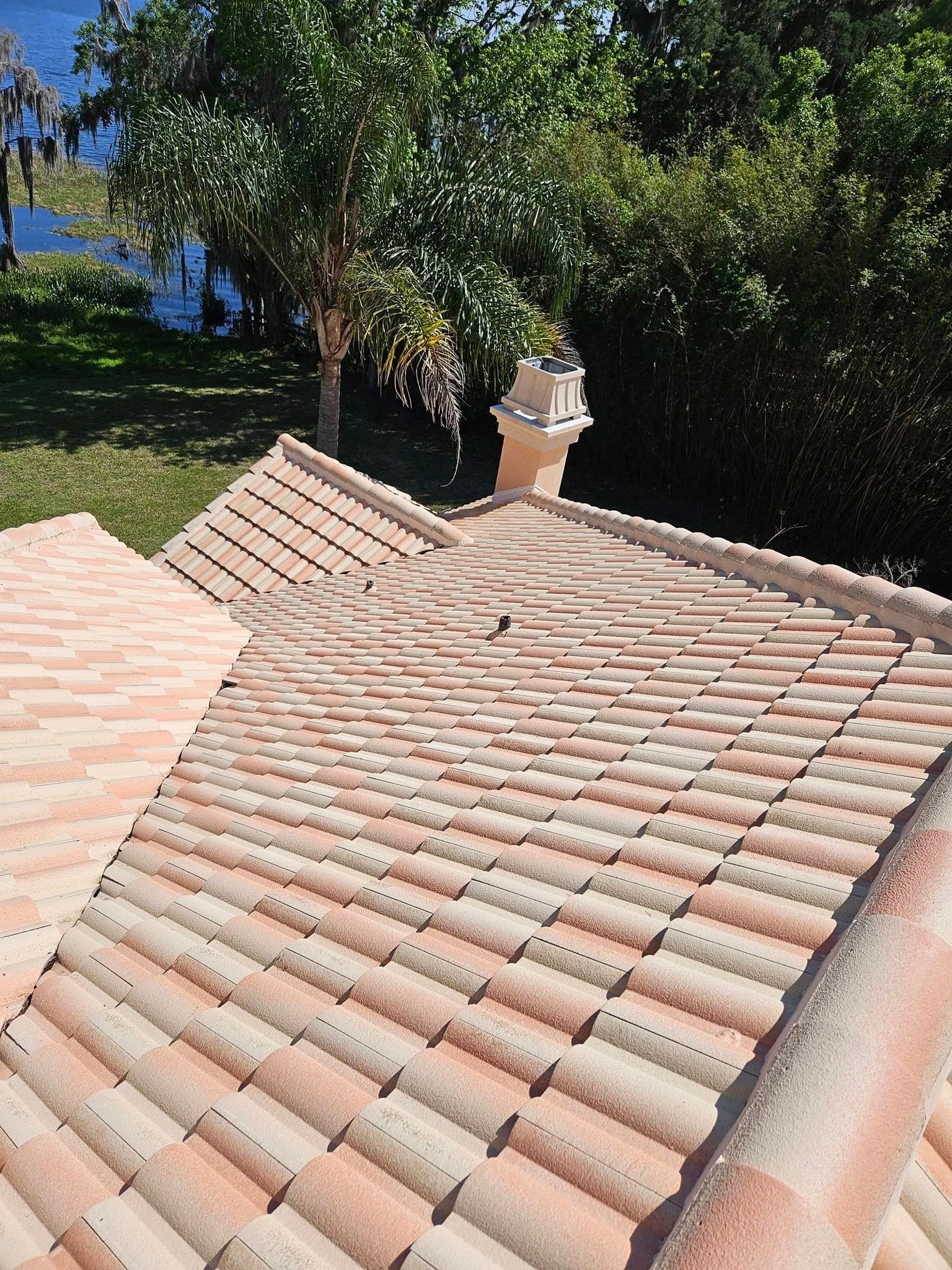 A tiled roof with a chimney on top of it and trees in the background.