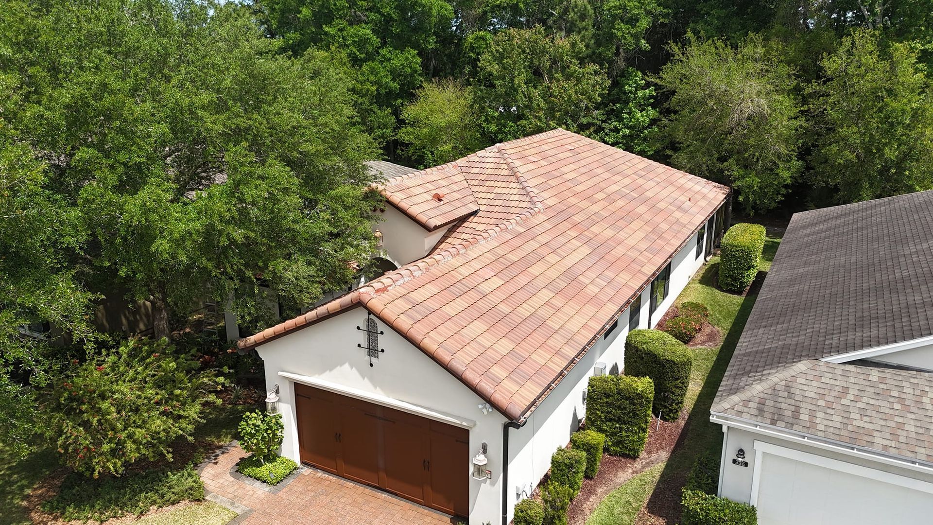 An aerial view of a house with a tiled roof and a garage surrounded by trees.