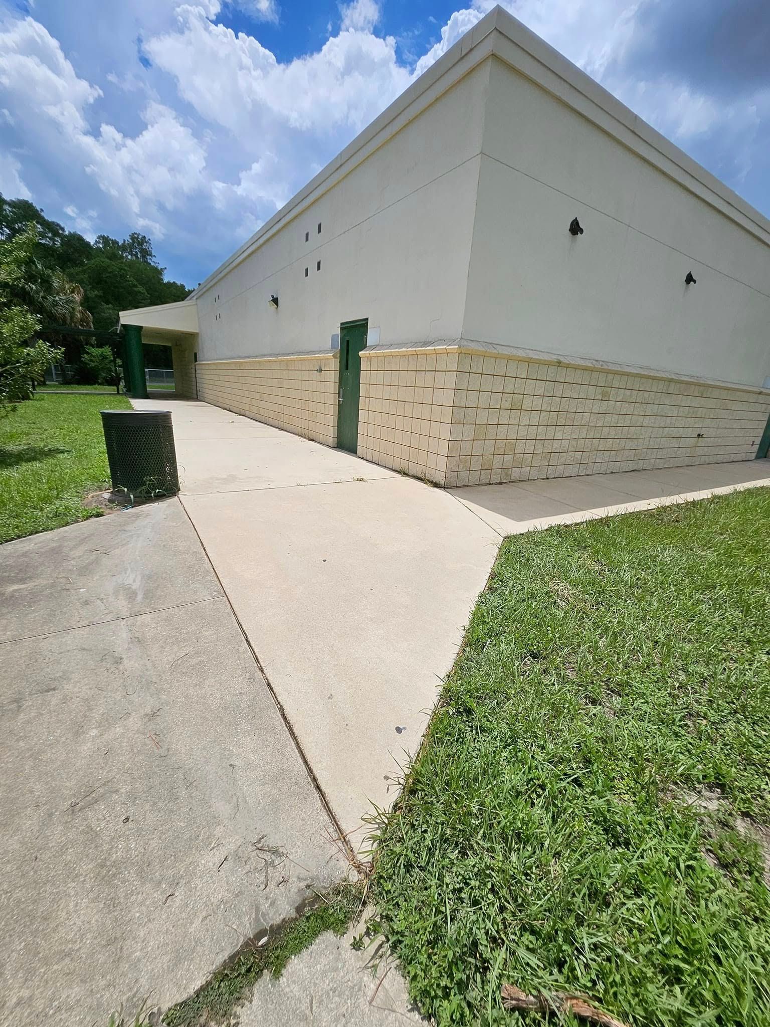 A white building with a green door is surrounded by grass and trees.