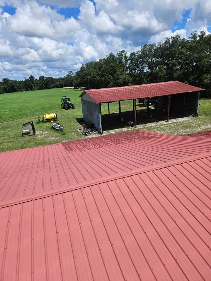 An aerial view of a barn with a red roof and tractors in the background.