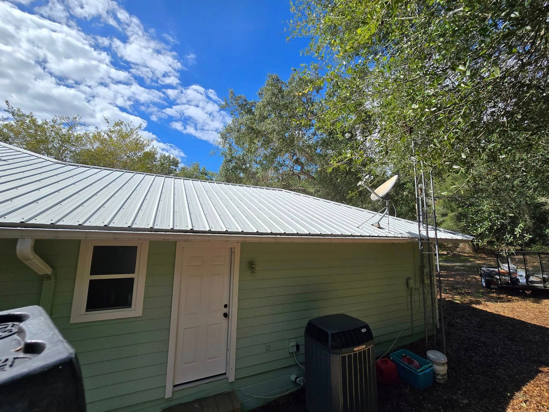 A green house with a white metal roof and a satellite dish on the roof.