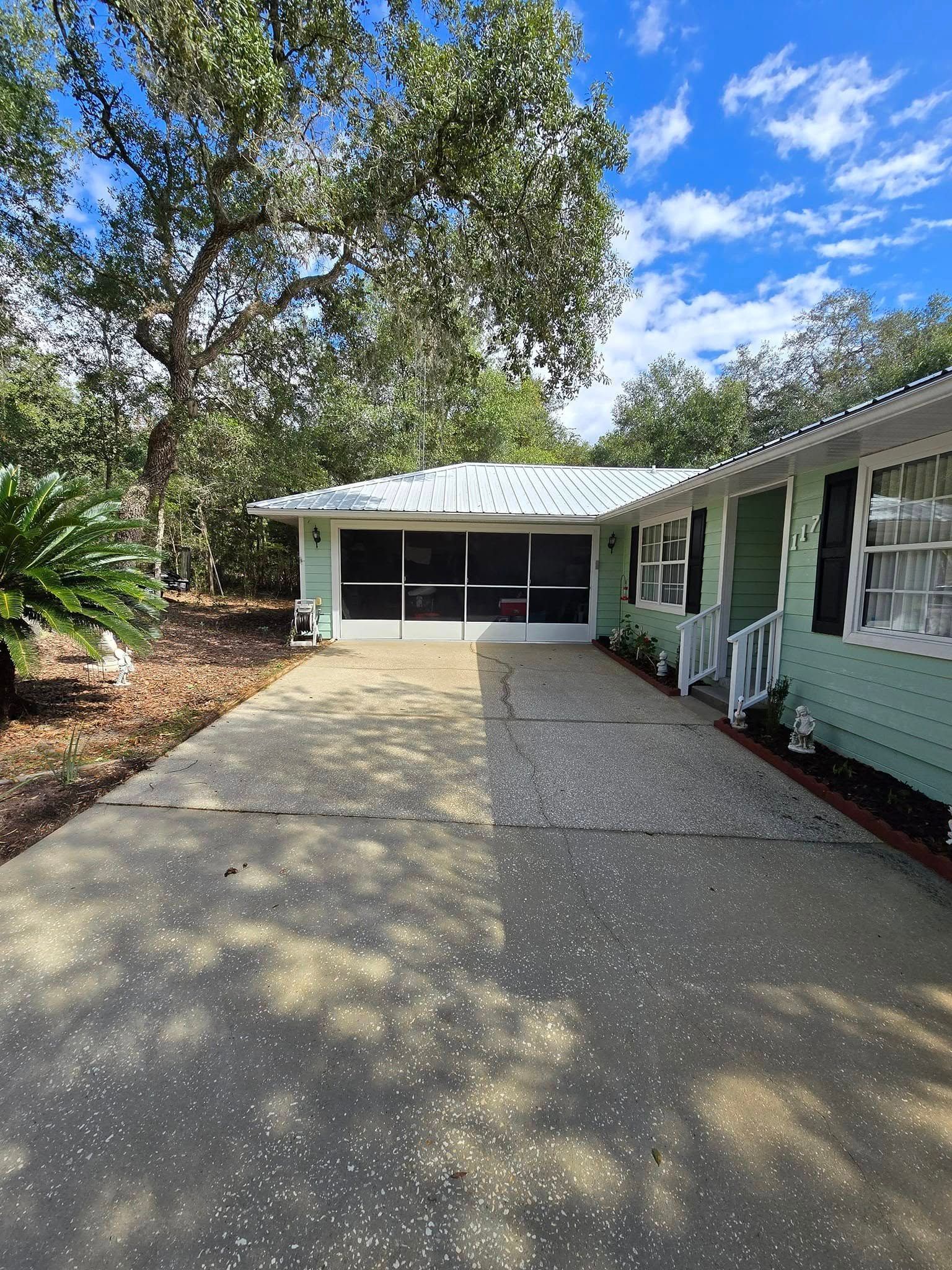 A green house with a white roof and a driveway leading to it.