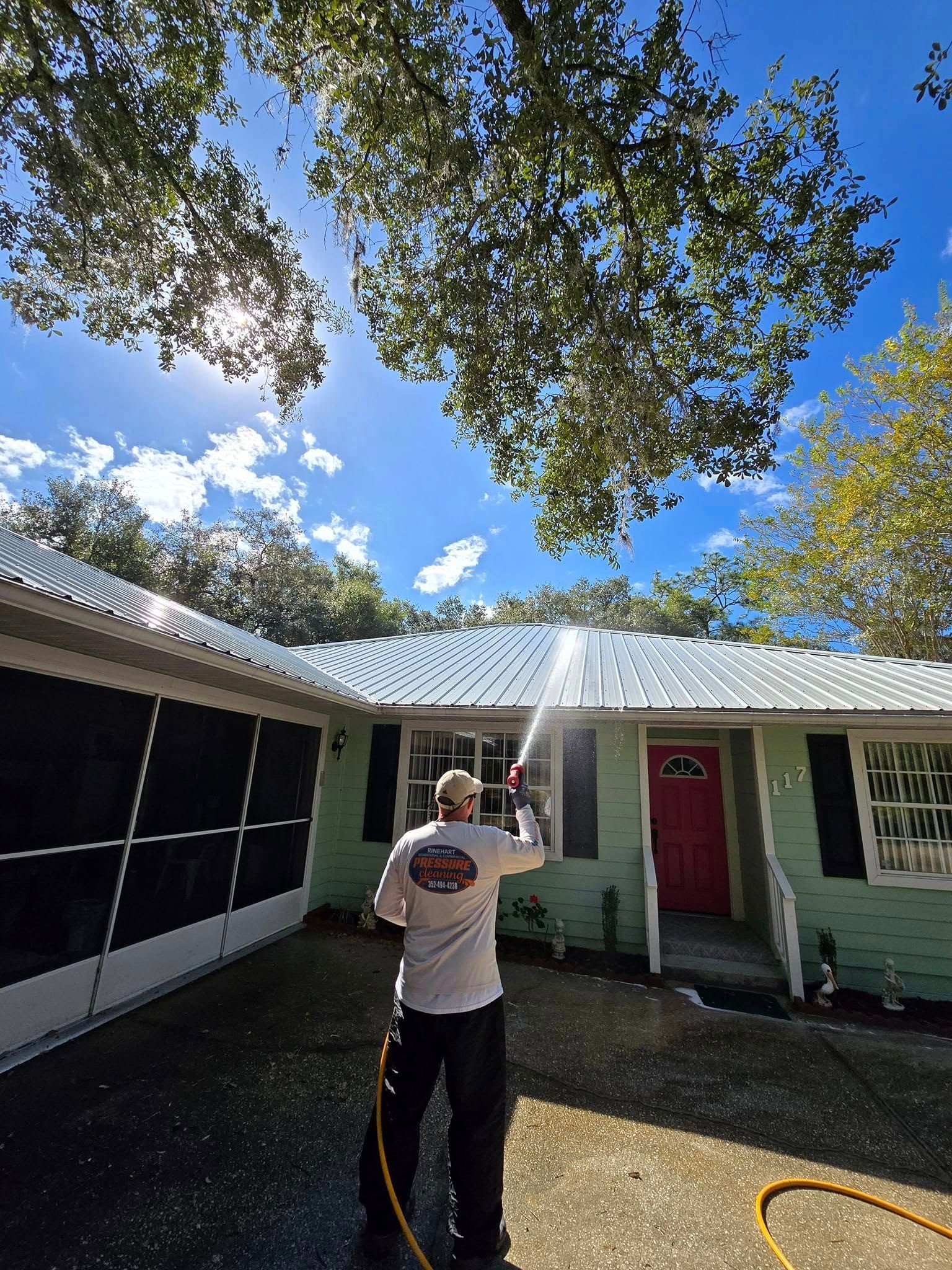A man is cleaning the roof of a house with a hose.