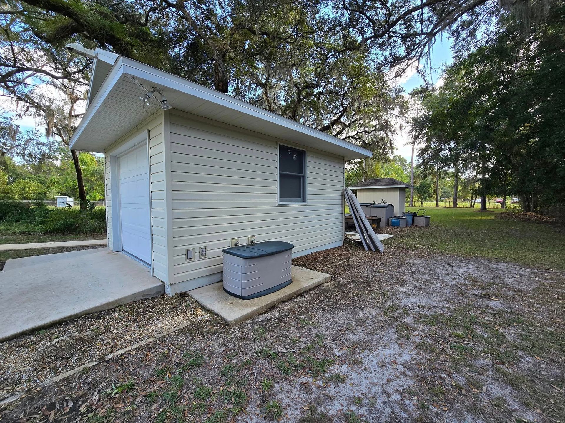 A small white shed with a generator in the backyard.