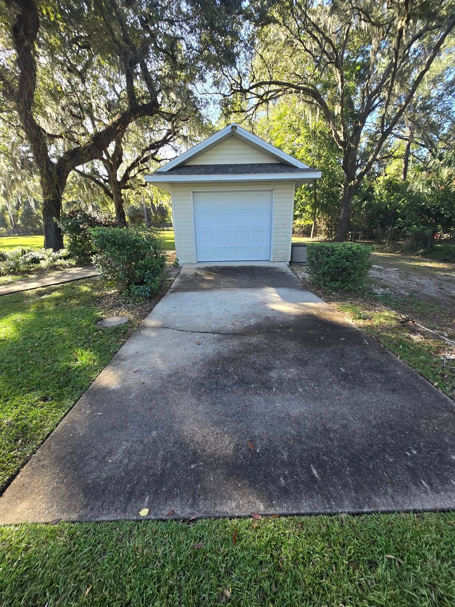 A small white garage is sitting in the middle of a driveway.