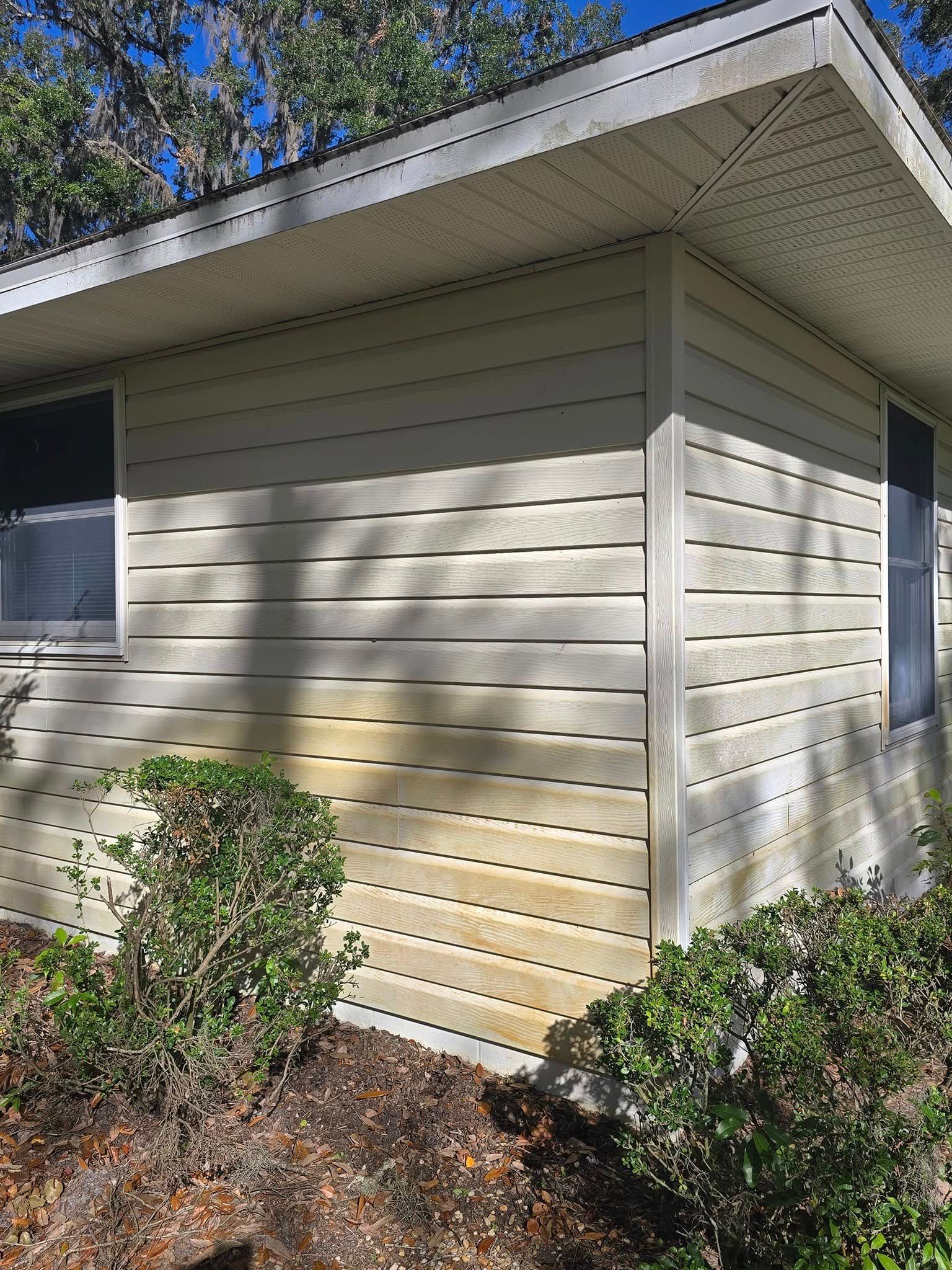 A white house with a roof and siding is surrounded by bushes and trees.