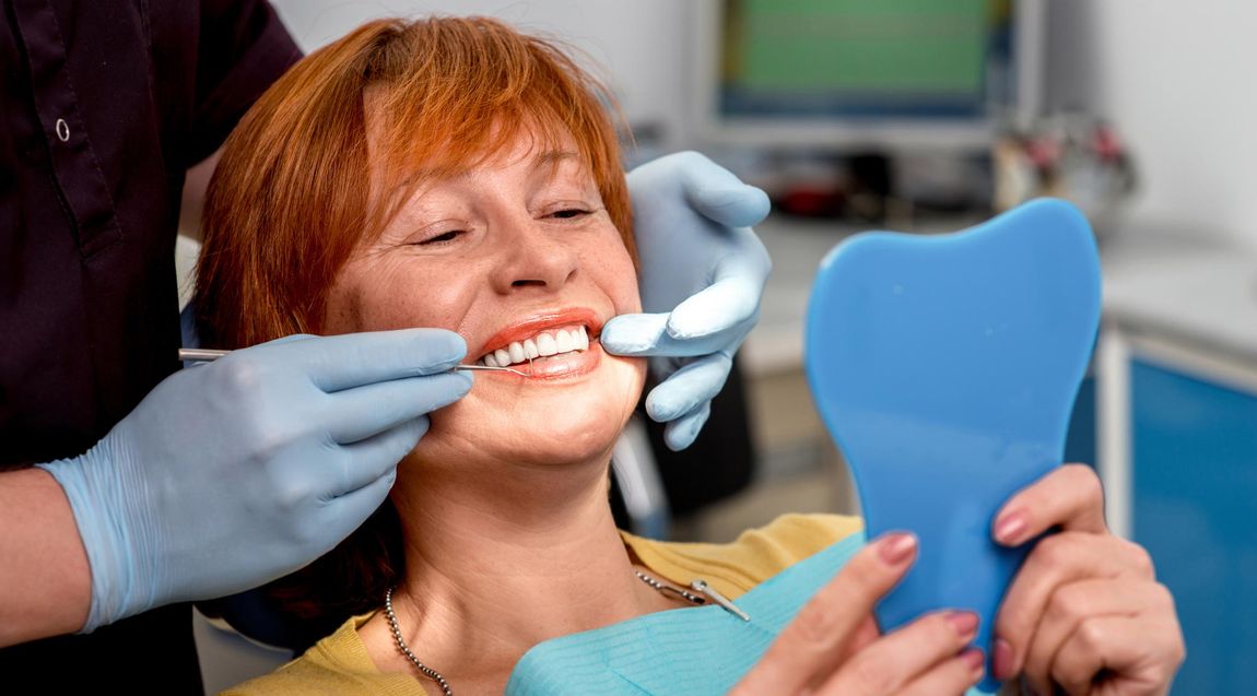 red haired lady looking at teeth in dental chair