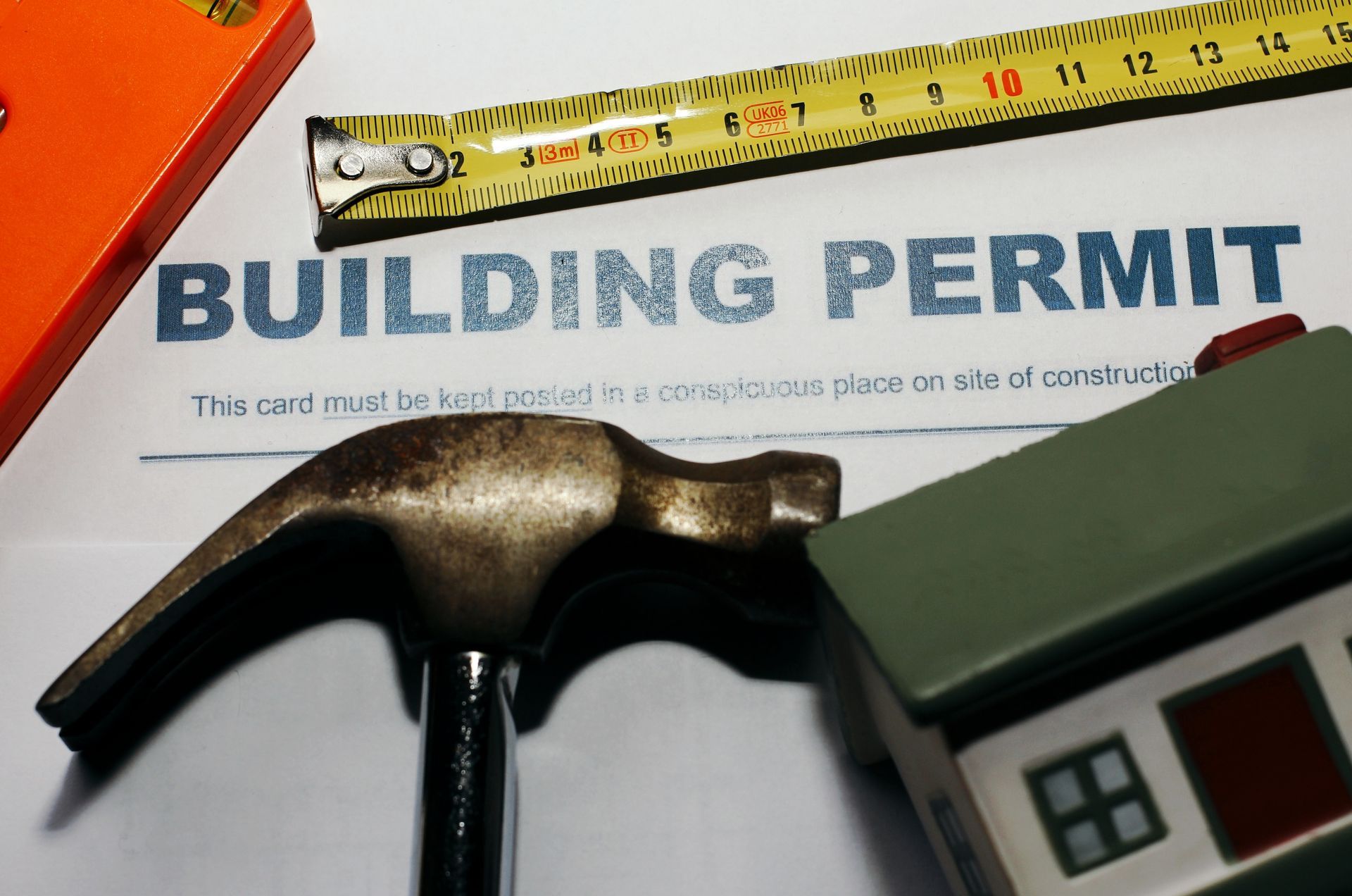 Image of a building permit with a hammer, tape measure, and model sitting on top of the permit.