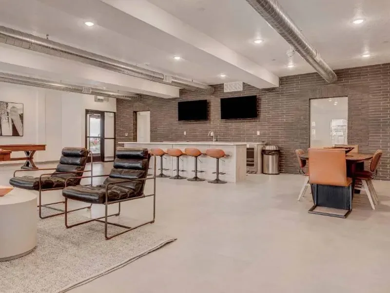 Modern community lounge with brick accent wall, bar seating, and lounge chairs.