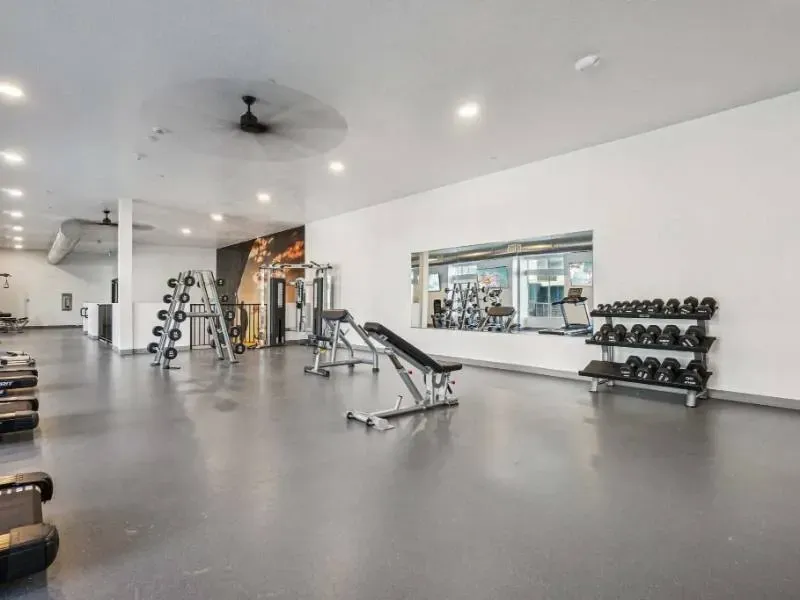 Spacious fitness center with dumbbells on a rack, benches, and cardio machines along a mirrored wall.