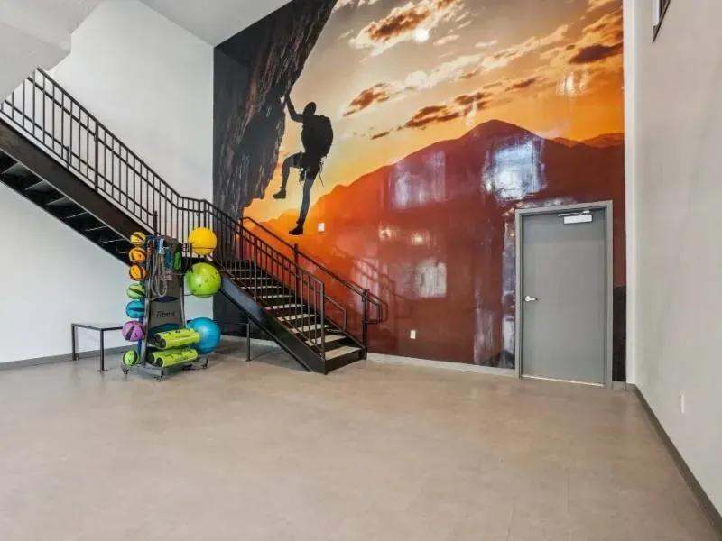 Indoor community gym area with stairs, a climber mural, and fitness equipment.