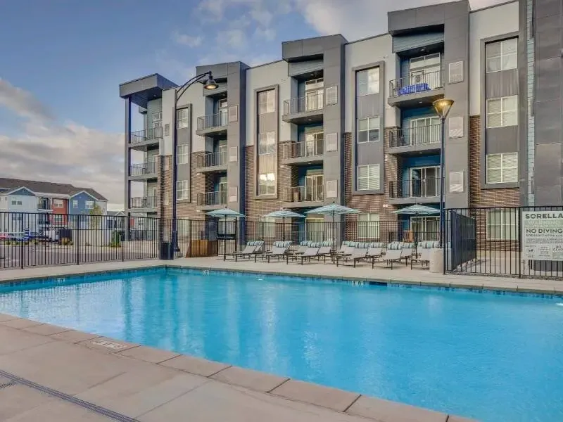 Outdoor rectangular swimming pool with lounge chairs and umbrellas at an apartment complex.