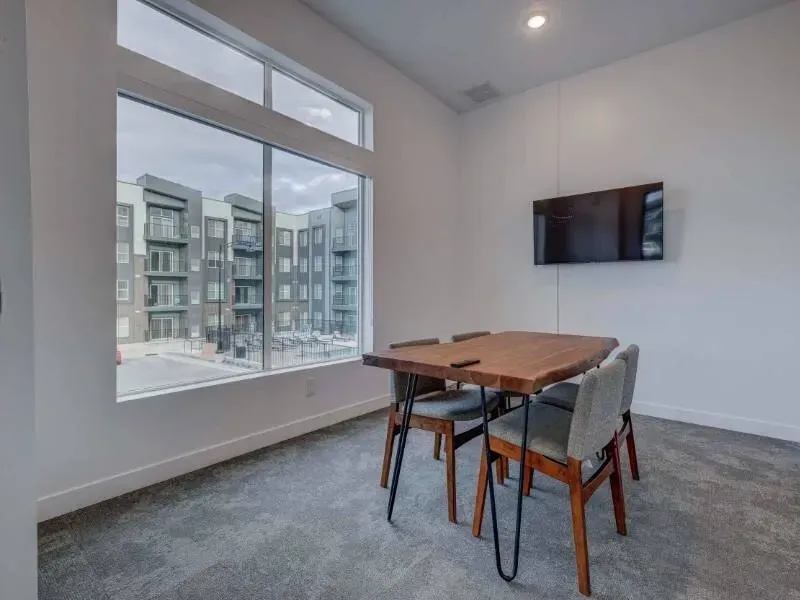 Amenity room with a large window, wooden table and chairs, and a wall-mounted TV.