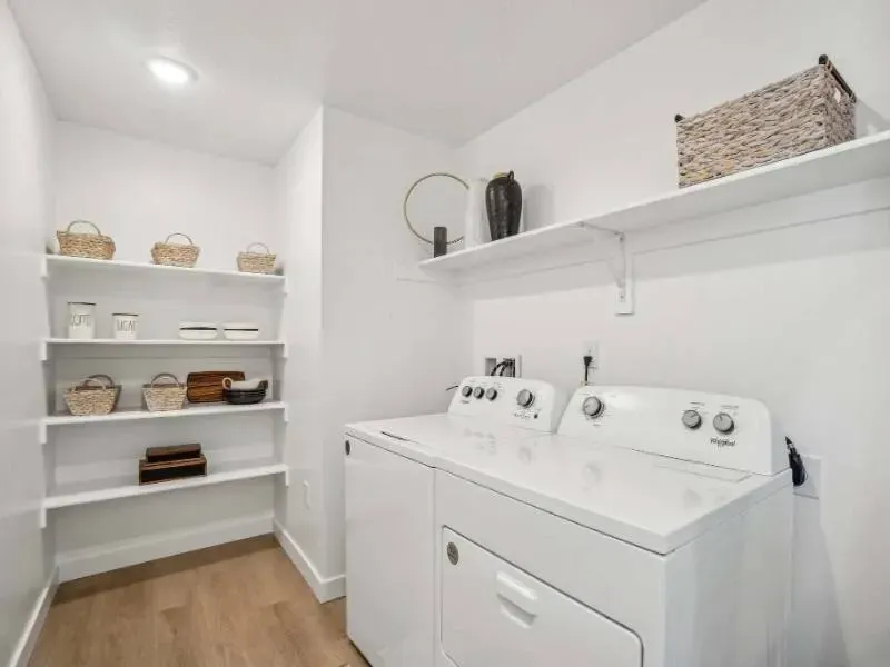 White washer and dryer in a bright laundry closet with open shelves and baskets.