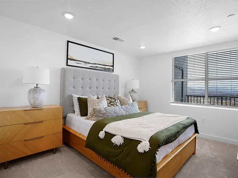 Bedroom in a modern apartment with a tufted headboard bed, two lamps, and a large window.