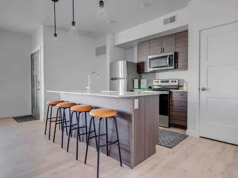 Modern kitchen with an island, bar stools, and stainless steel appliances in a bright apartment.