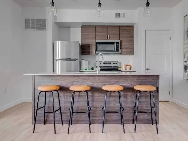Open-concept kitchen with island, stainless appliances, and four orange stools.