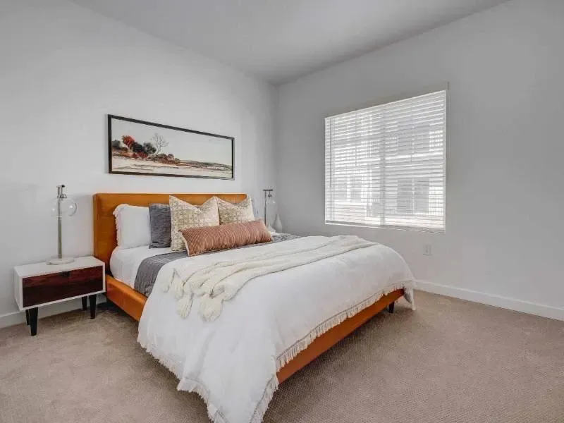 Bedroom with an orange upholstered bed, white bedding, two nightstands, and a window with blinds.