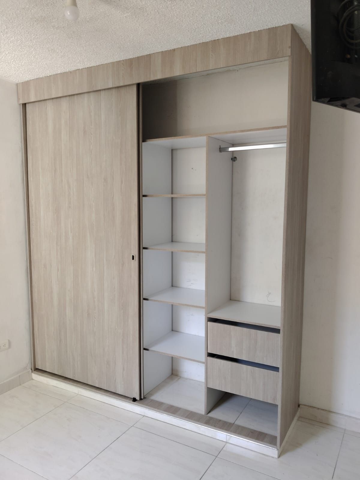 Armario con puertas corredizas de madera clara, parcialmente abierto, que deja al descubierto estantes y cajones.