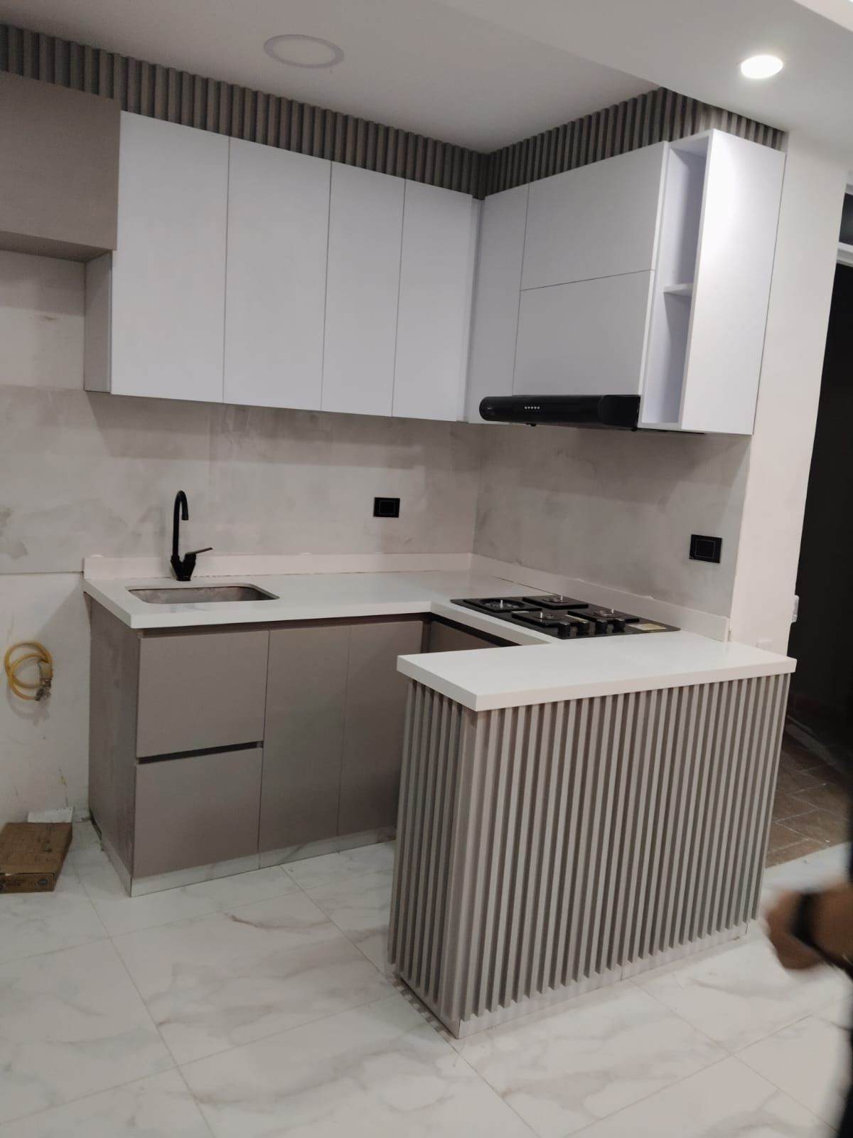 Cocina moderna con gabinetes blancos y grises, encimera y una pequeña isla con rayas verticales grises.